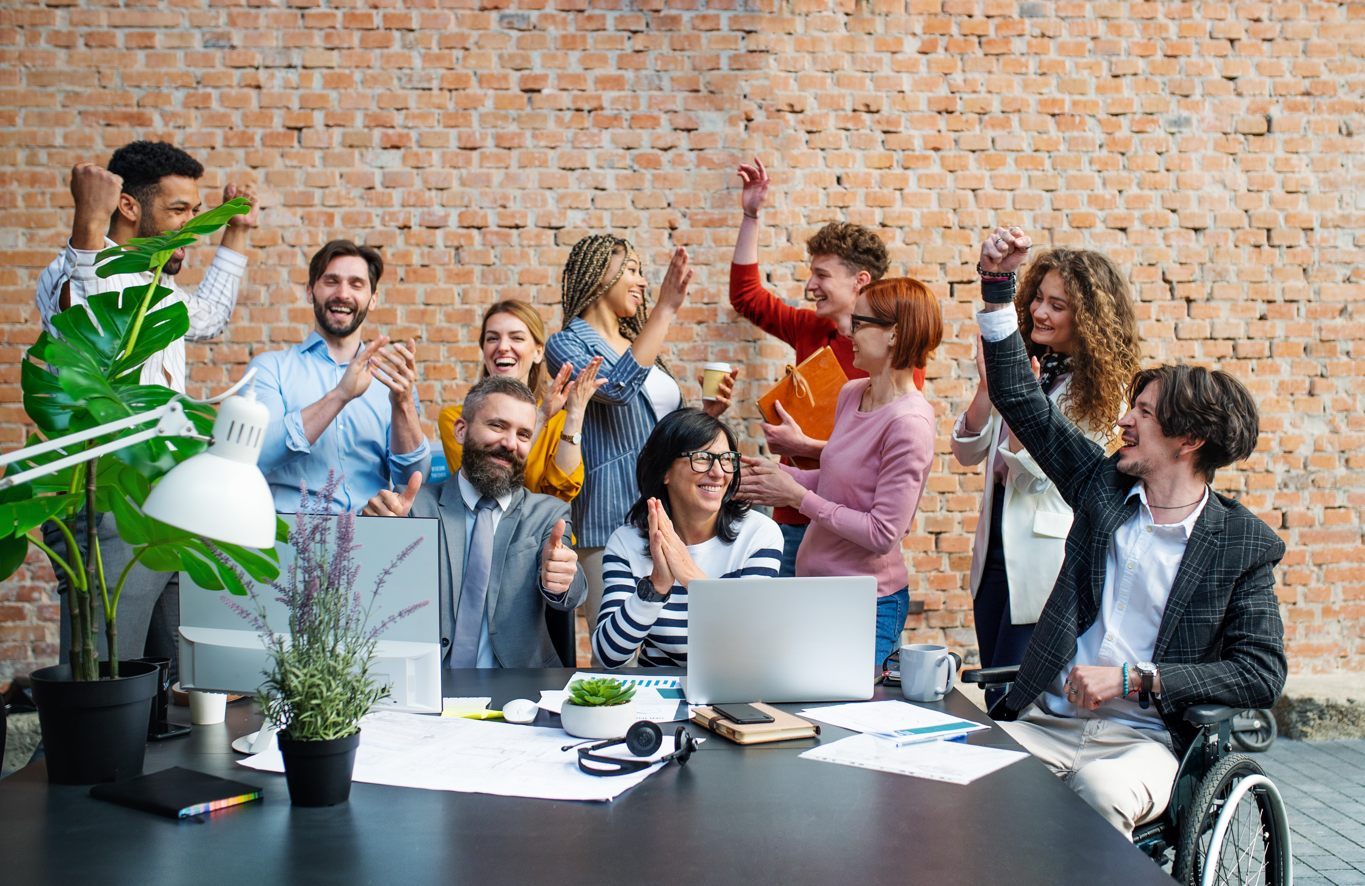 A diverse group of employees standing and sitting around a conference table high-fiving and cheering each other.