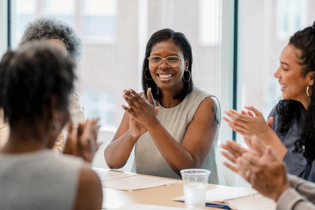 A group of employees sitting around a conference table and applauding.