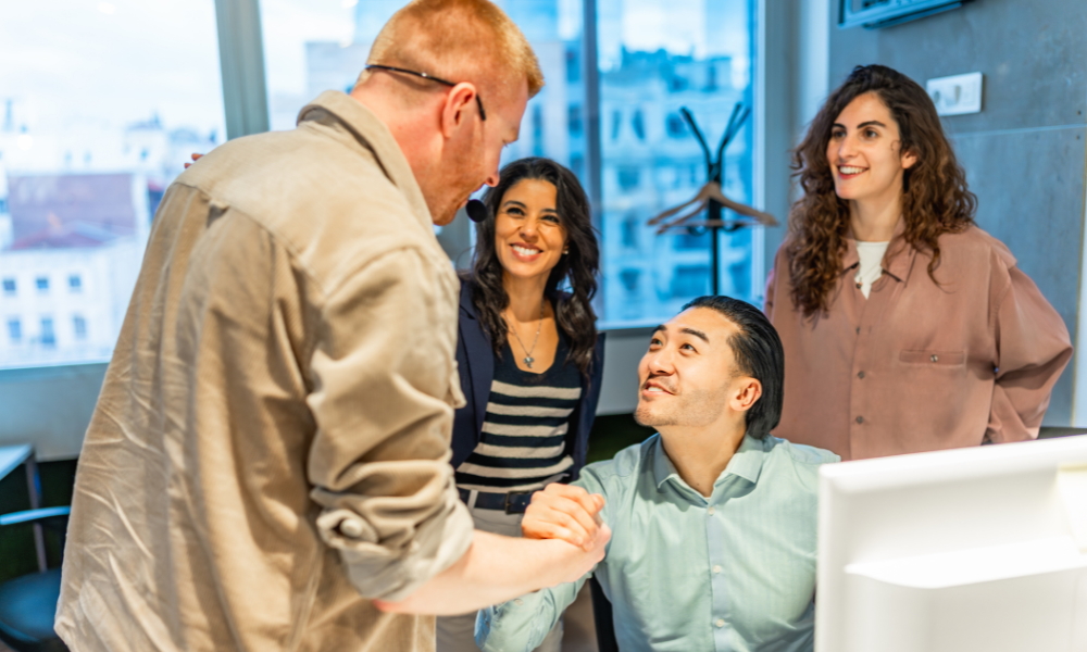 Business team congratulating their colleague on a successful project, shaking hands in the office workplace