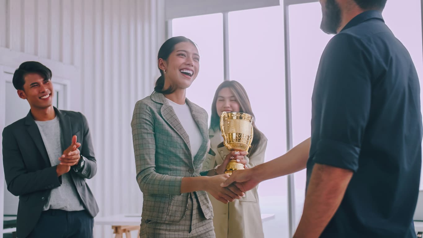 A woman being applauded by peers in the office as she receives an award.