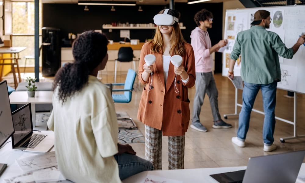 Two women using a VR headset in a conference room while two men write on a white board.