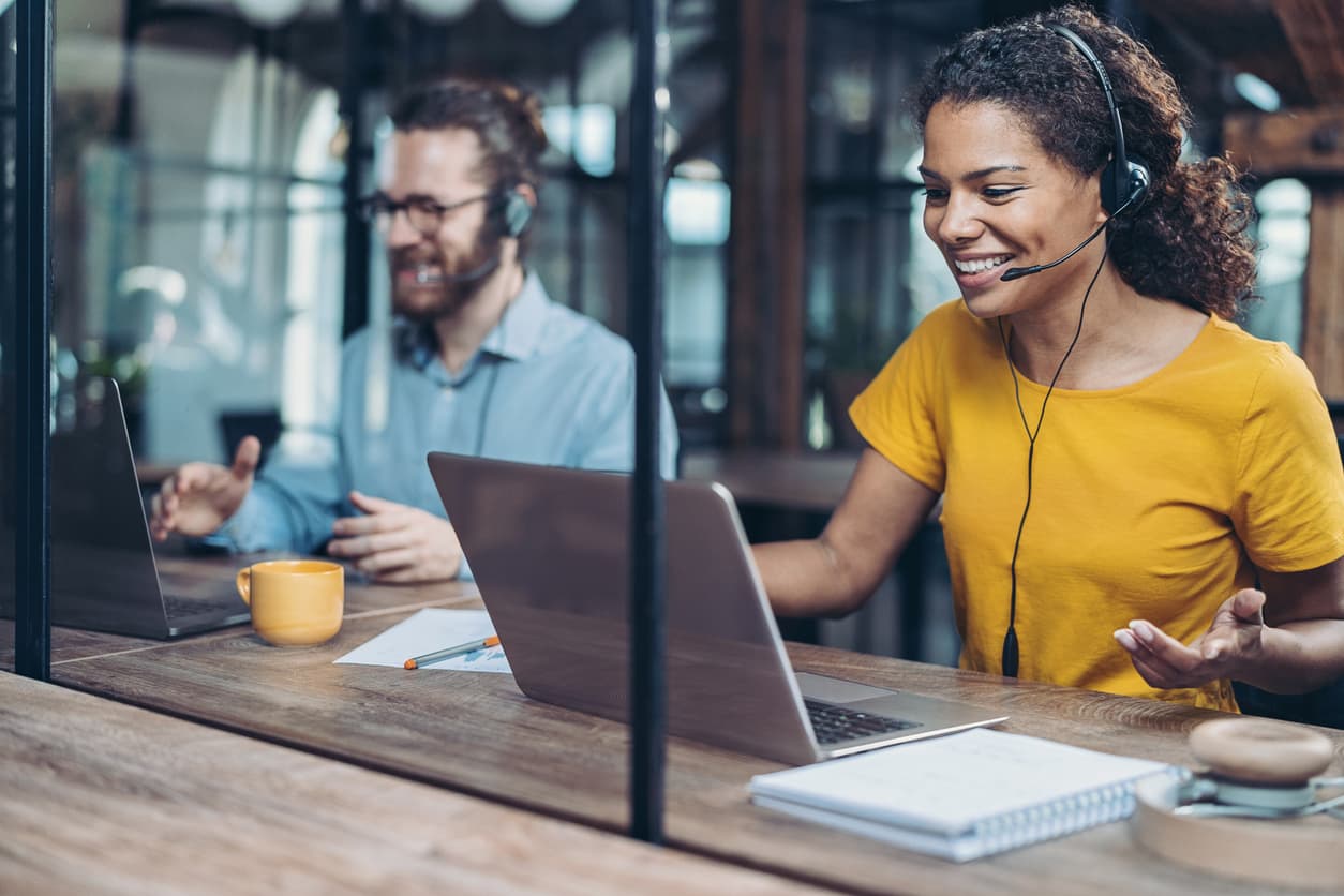 Two customer care professionals at a help desk with their laptops and notebooks