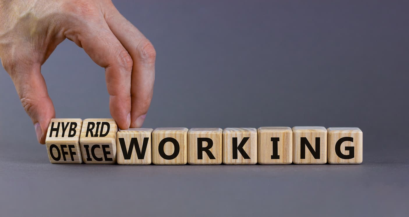 A hand laying out a row of dice that spell out the words “hybrid” “office” and “working.”