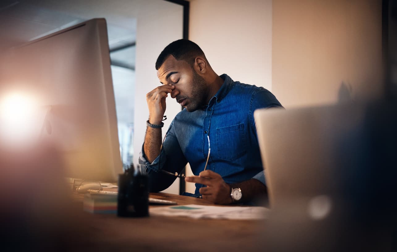 Employee suffering from burnout rubbing their eyes in frustration in front of a work computer.