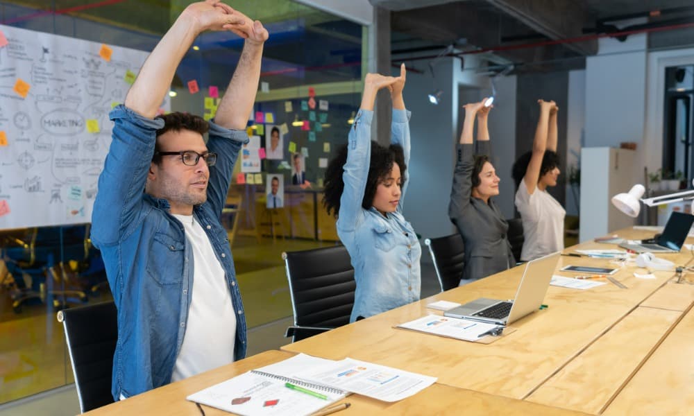 A group of employees sitting at their workstation doing yoga stretches together.