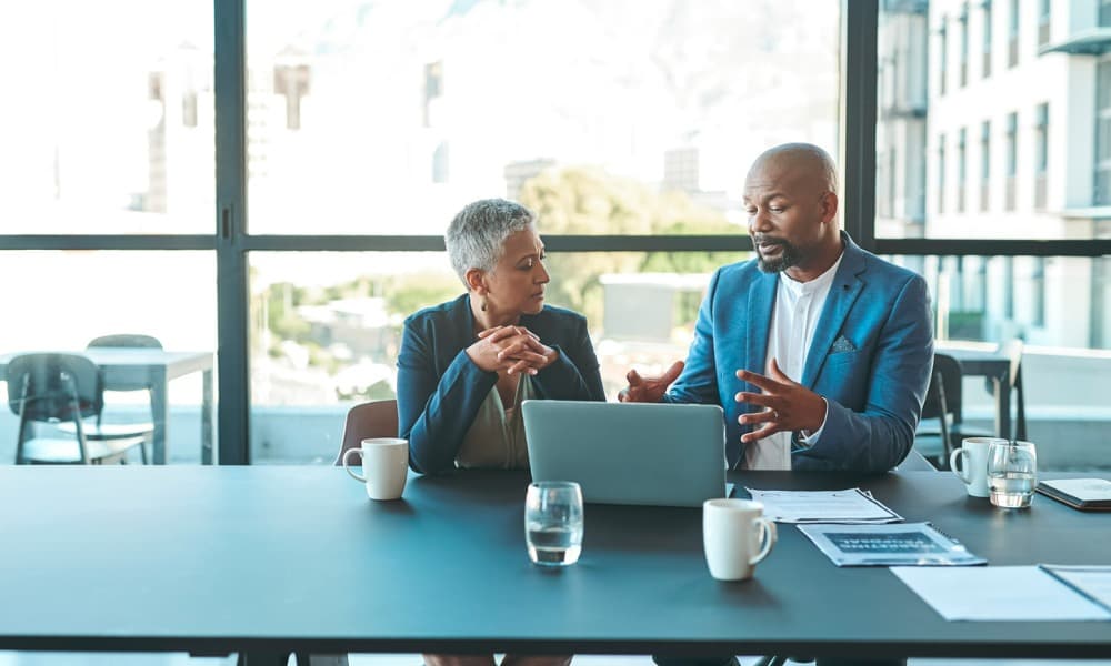 A manager with a laptop having a one-on-one meeting with an employee.